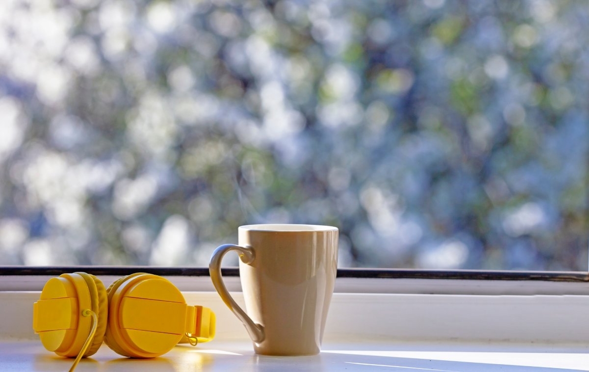 image showing a pair of headphones and a mug in front of a window