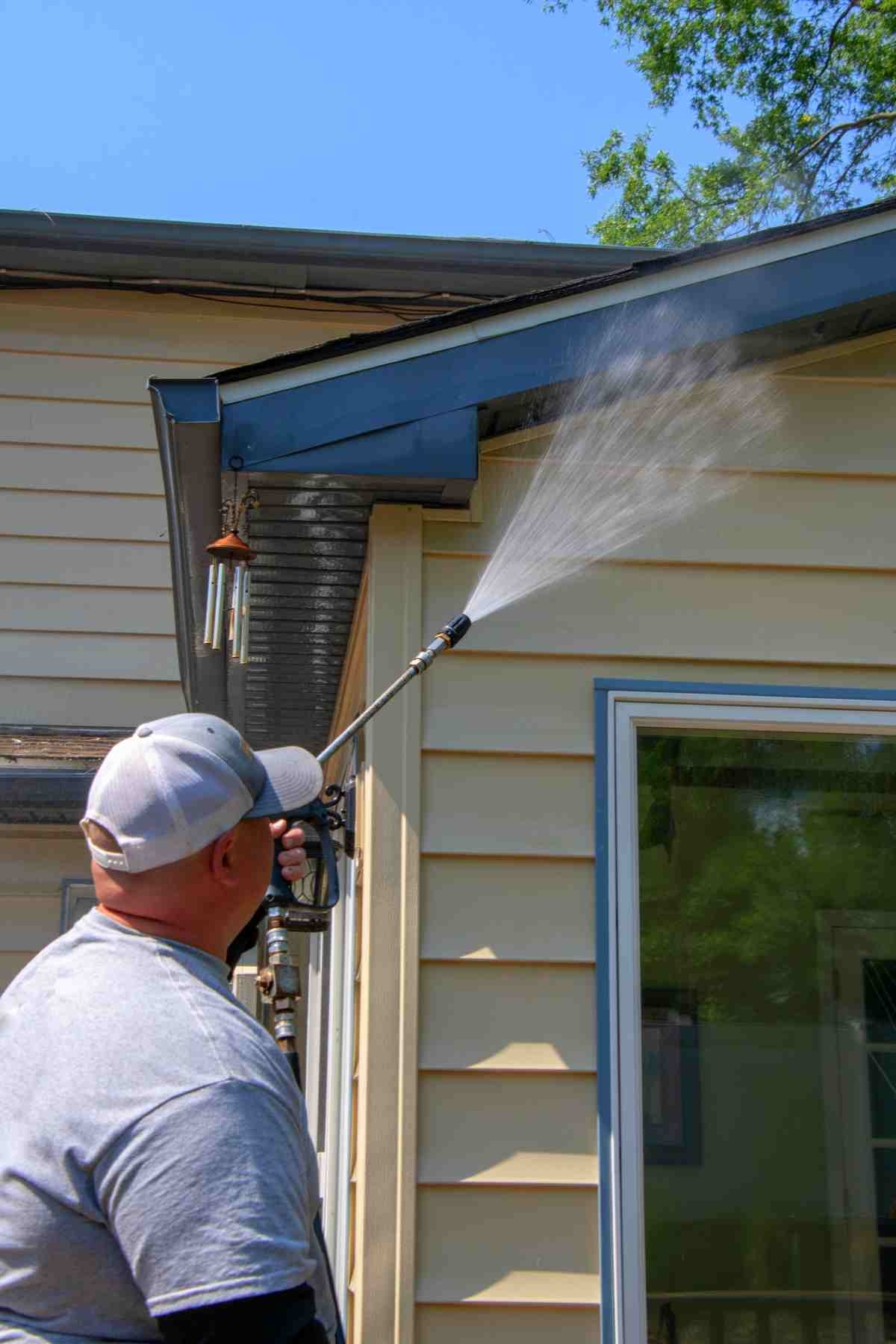 image showing a man cleaning the siding of his house