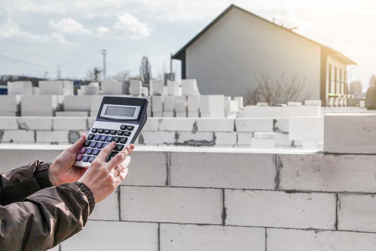 image showing hand with calculator while on the background there is a house and some bricks