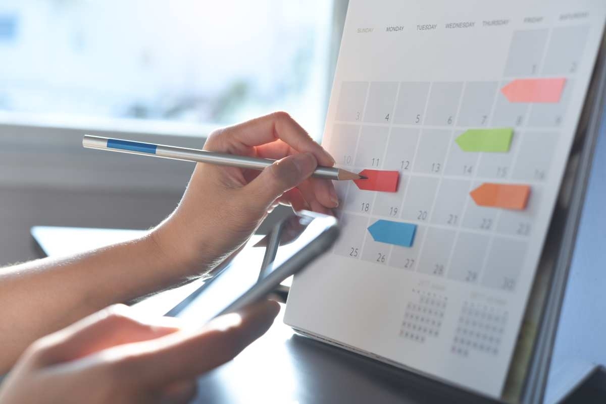 image showing a hand writing with a pencil on a post it sticked to a table calendar