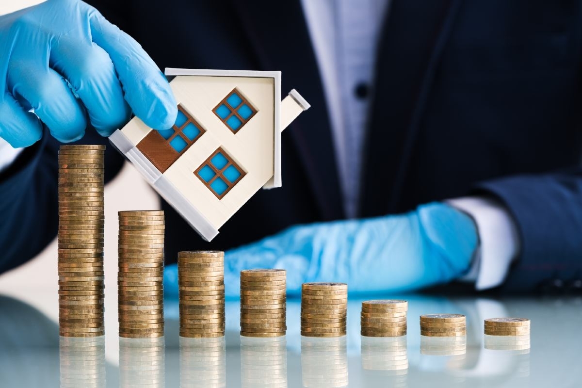 image showing two hands holding a small house miniature against a descending pile of coins