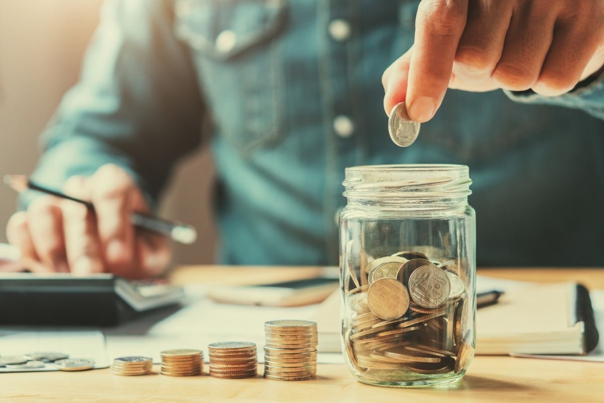 image showing person putting coins in a jar while using a calculator