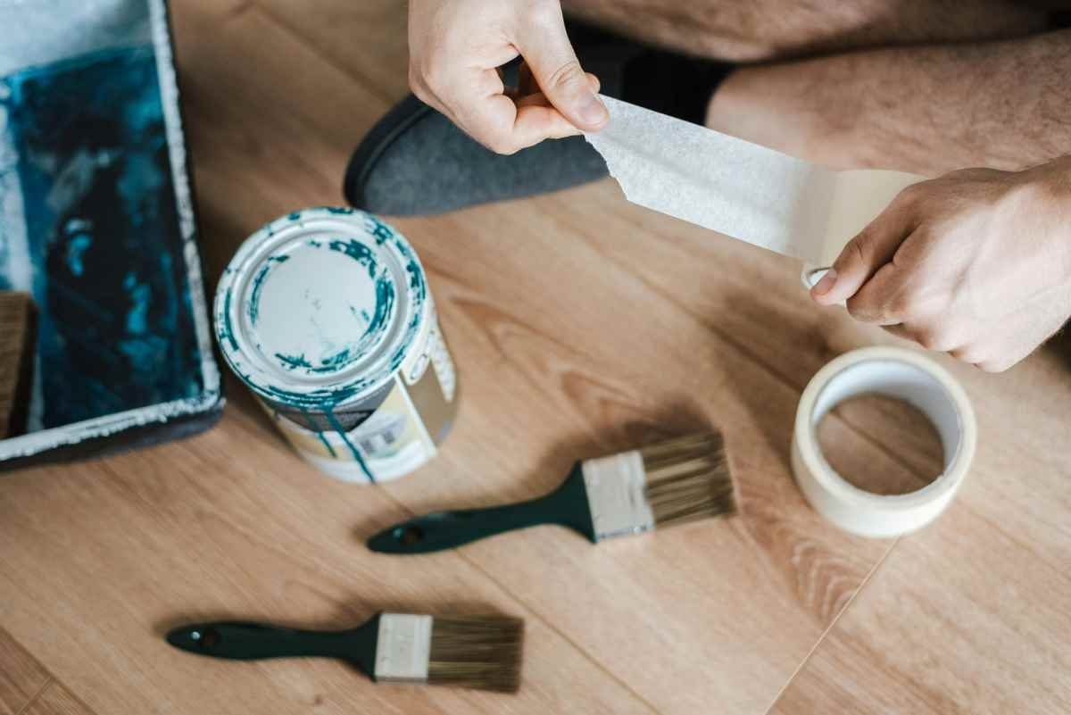 someone sitting ready to paint, next to a can of painting, brush and tape in his hands