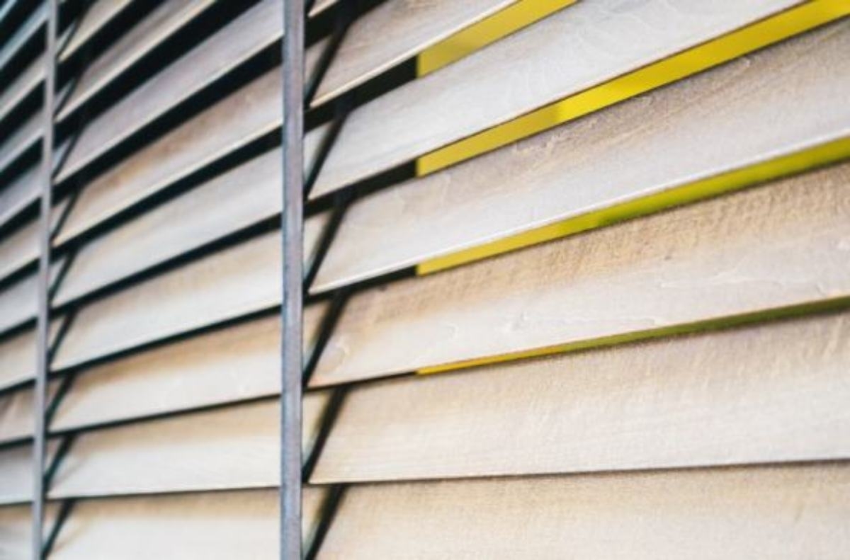 Wooden window blinds, partially closed, contrasted with sunlight.