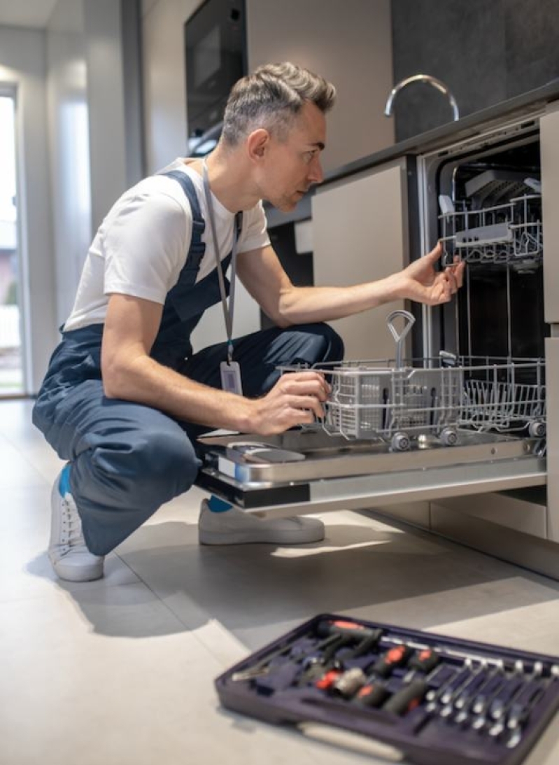 Man repairing a dishwasher with tools, addressing kitchen appliance malfunction.