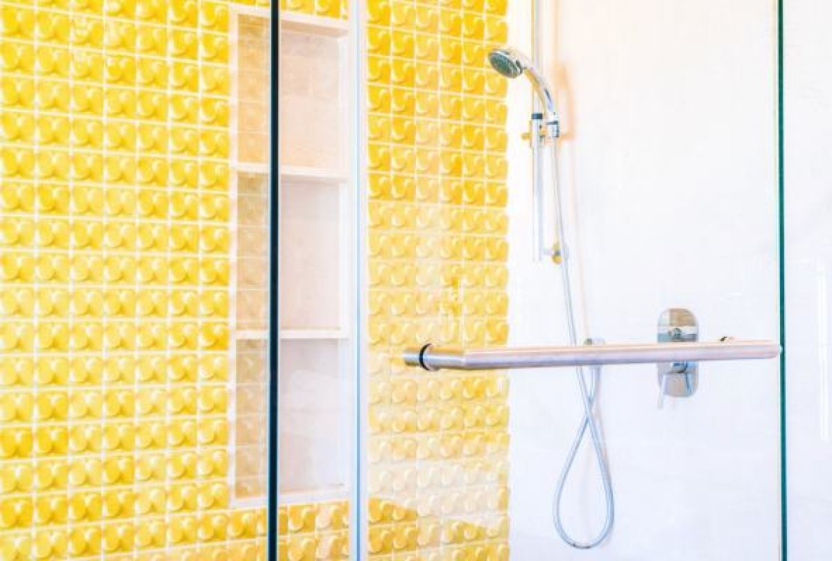 Close-up of a hinged shower door handle in a modern bathroom. The yellow wall behind the handle suggests the door opens outward.